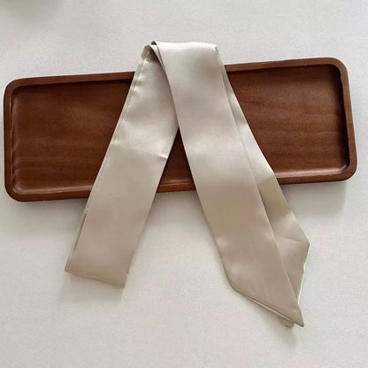 Beige satin scarf draped over a wooden tray on a light background