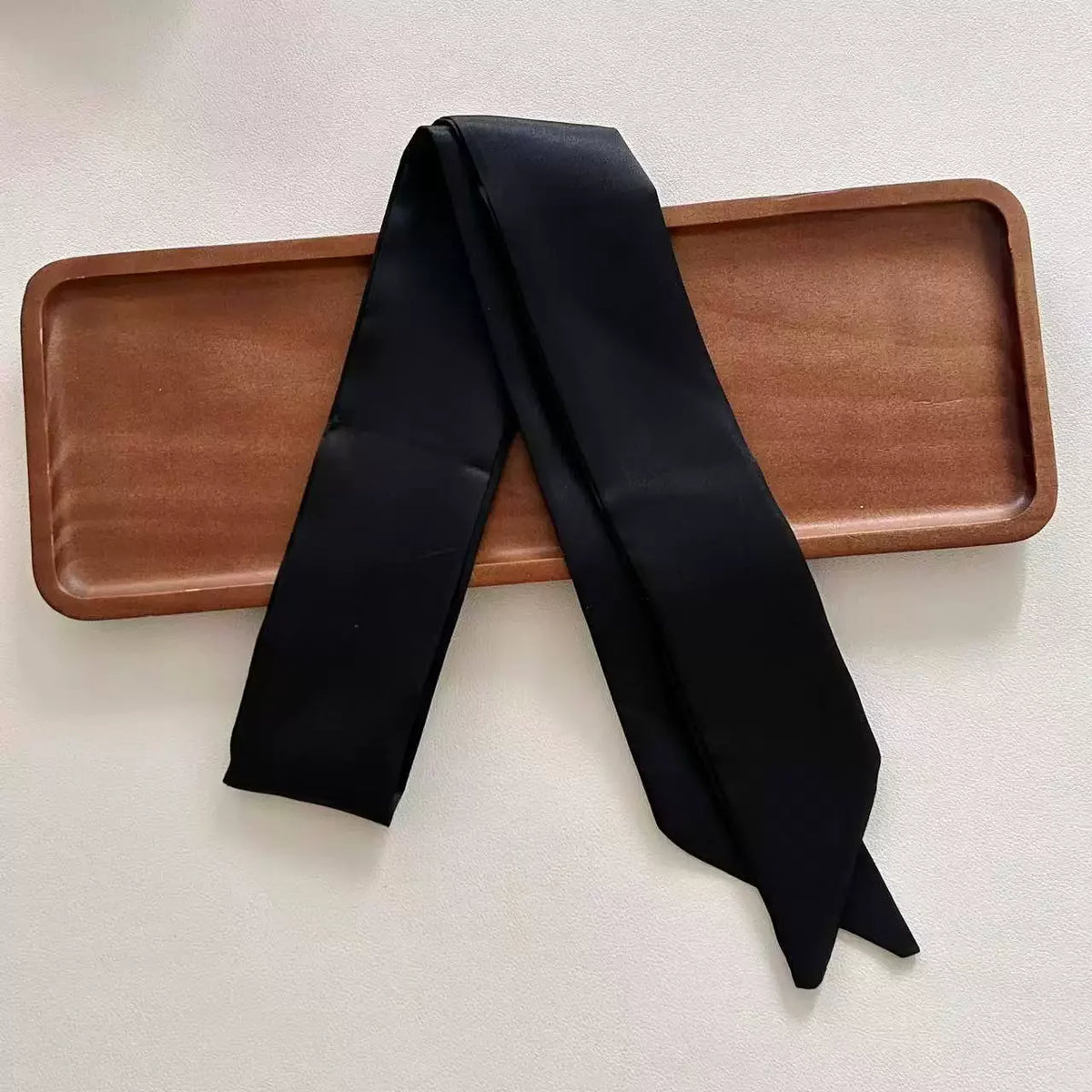 Black scarf draped over a wooden tray on a light background