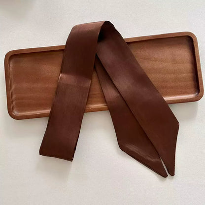 Coffee skinny satin ribbon scarf draped over a wooden tray on a light background