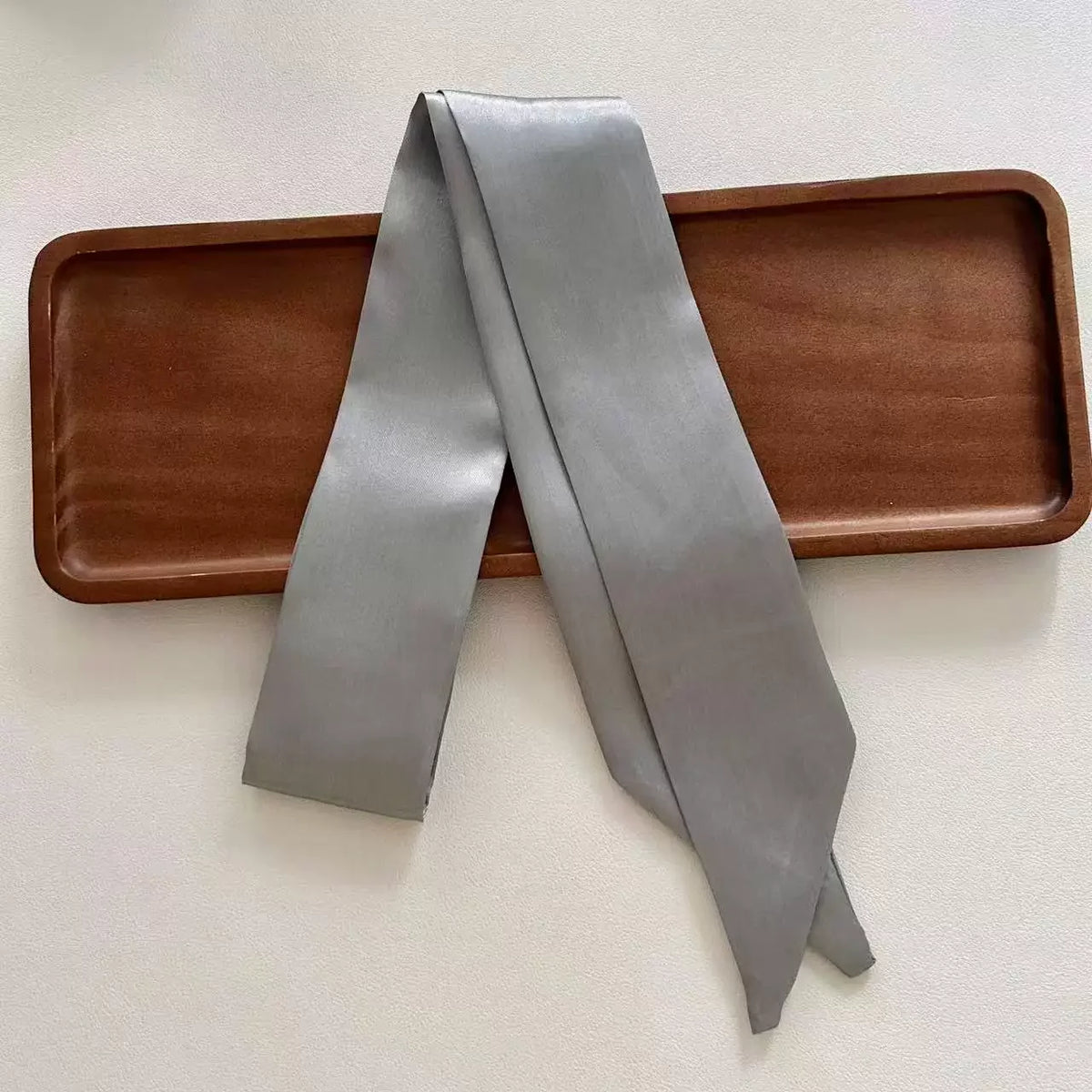 Gray scarf draped over a wooden tray on a light background