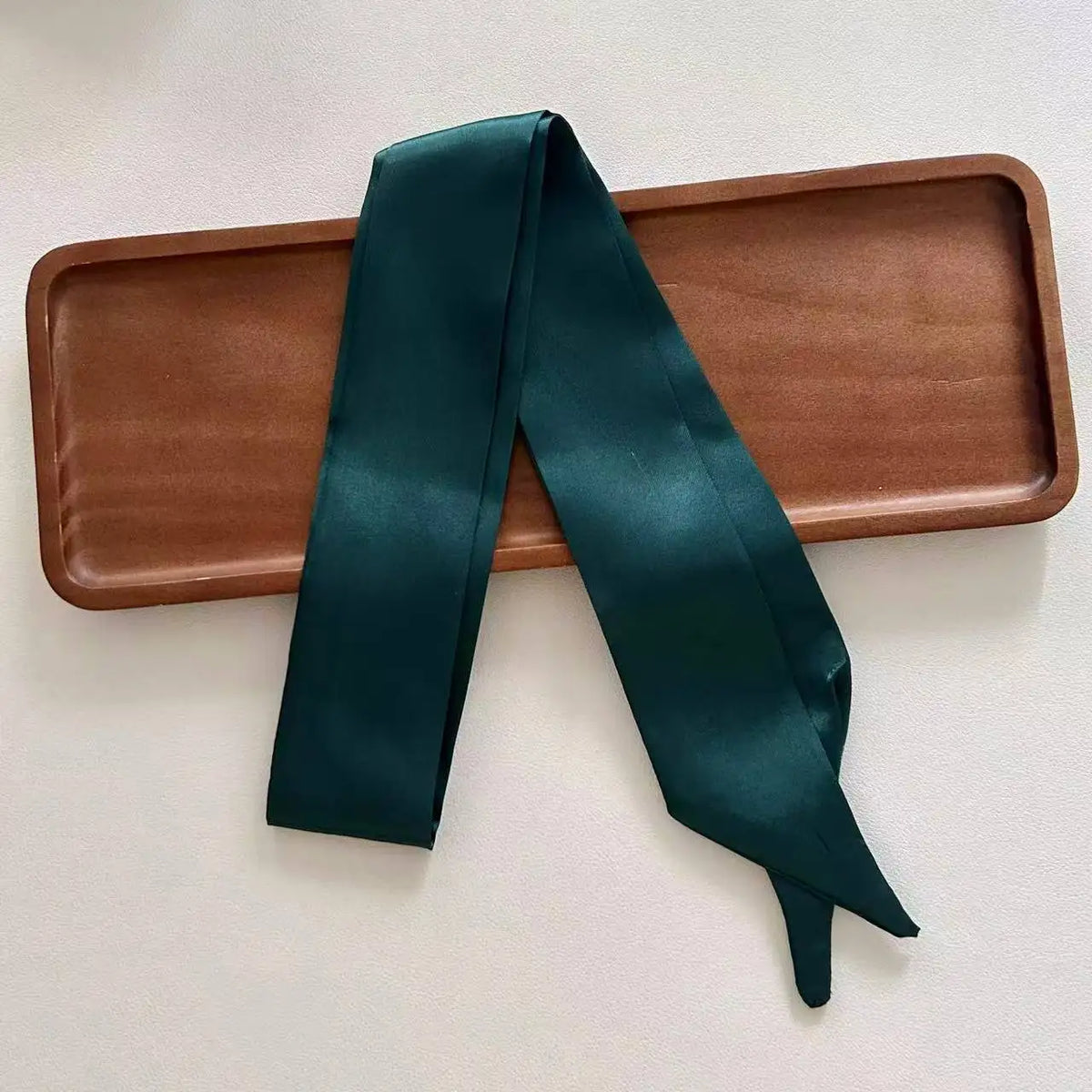 Green satin scarf draped over a wooden tray on a light background