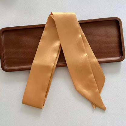 Khaki skinny satin ribbon scarf draped over a wooden tray on a white background