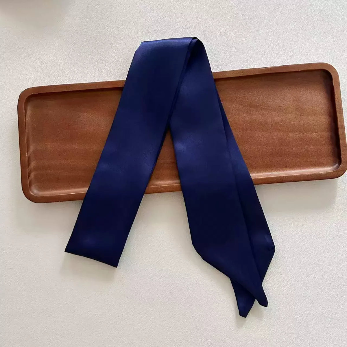 Navy blue satin scarf on a wooden tray with a white background