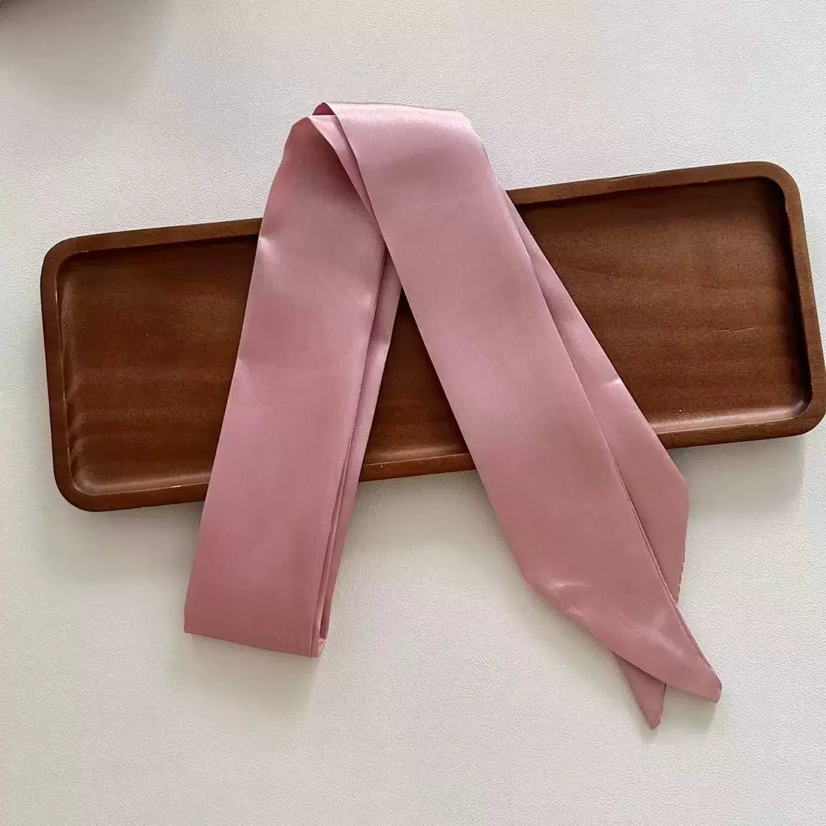 Pink satin scarf draped over a wooden tray on a light background