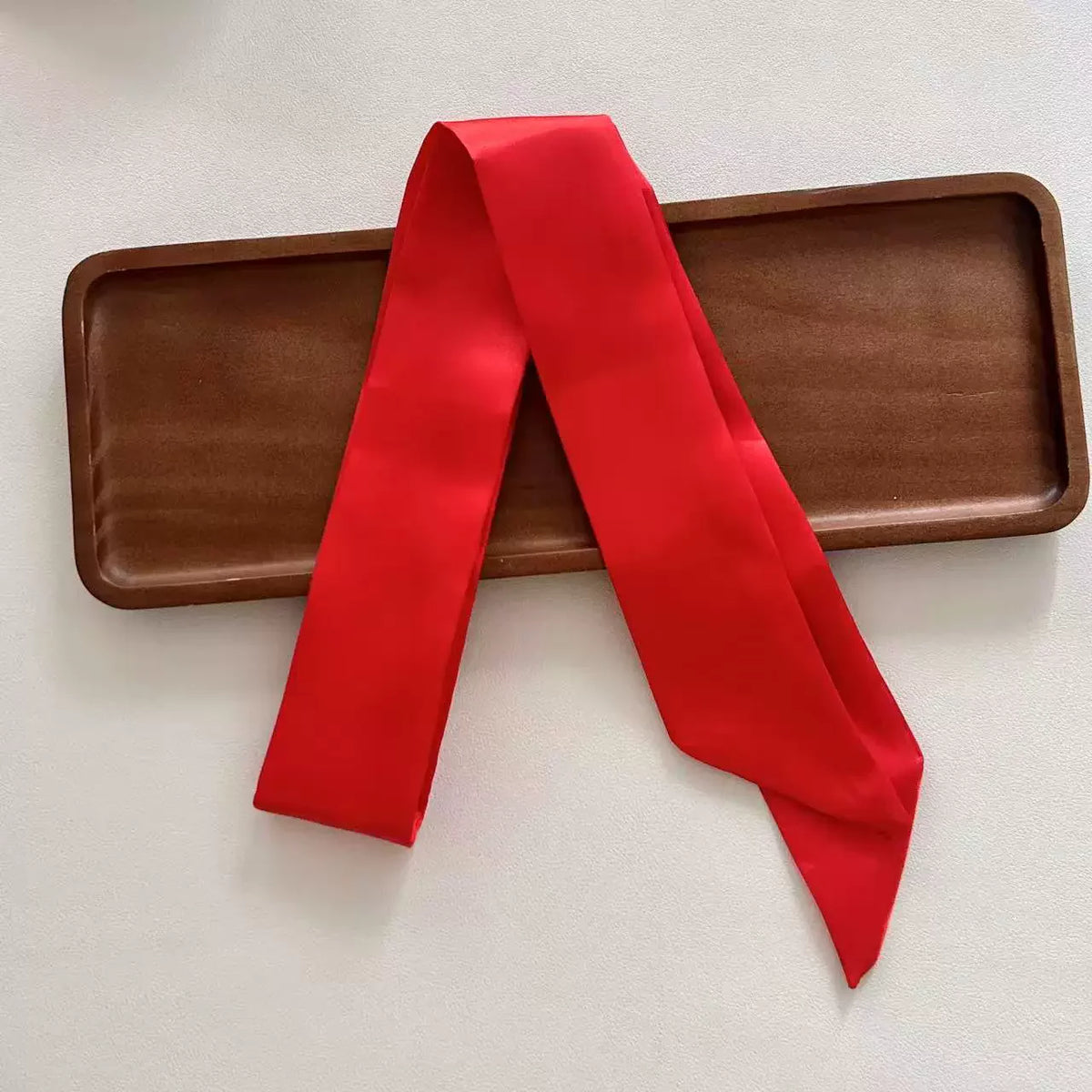 Red scarf draped over a wooden tray on a light background