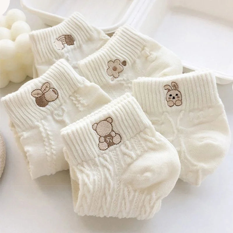White knit ankle socks with bear, rabbit and decorative motifs shown in a close-up.