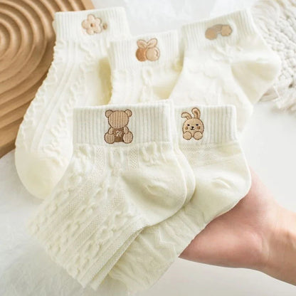 White textured ankle socks with bear and rabbit cuff motifs held in a hand.