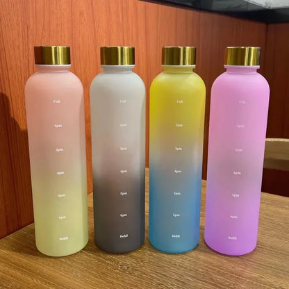 Four gradient-colored water bottles with gold lids on a wooden surface.