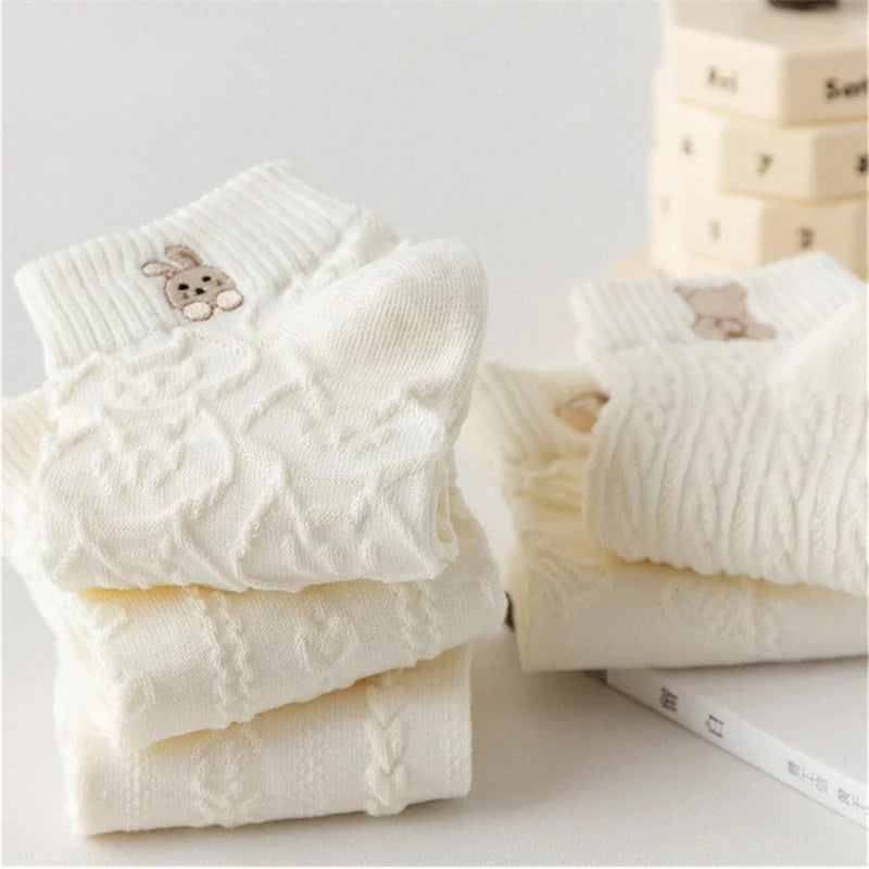 Folded white knit ankle socks stacked on a light surface, with a rabbit motif on the top sock.