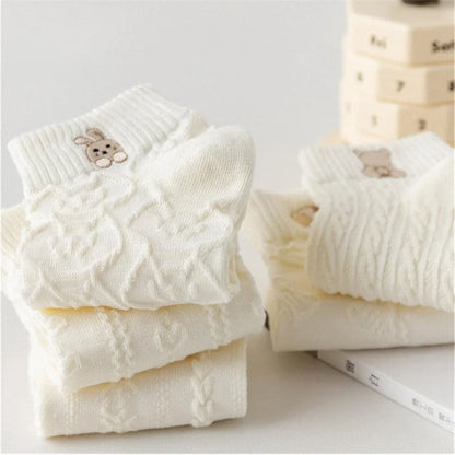 Folded white knit ankle socks stacked on a light surface, with a rabbit motif on the top sock.