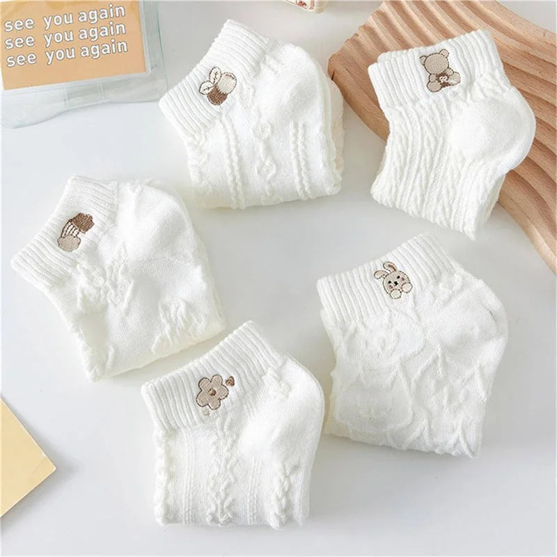 Folded white knit ankle socks with small cartoon motifs arranged on a light surface.