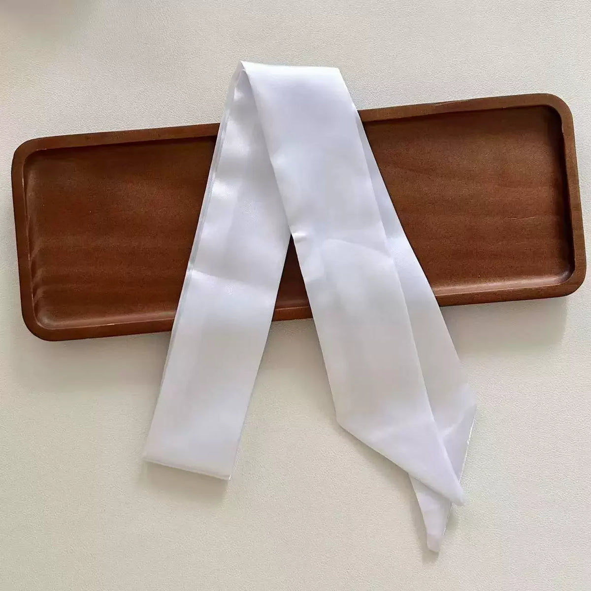 White skinny satin ribbon scarf on a brown tray with a white background